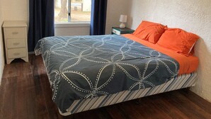 Ein Schlafzimmer mit Bett, Nachttisch, Schubladeneinheit und einem Fenster mit Vorhängen.