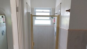 Een kleine, afgesloten douchecabine met een glazen deur, een raam erboven en een handdoekhouder aan de muur.
