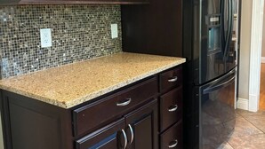A kitchen with dark wood cabinets, a granite countertop, and a black refrigerator. - Luxury Modern Stay - 2000 Sqft (Indianapolis)