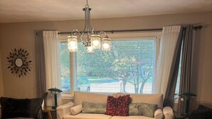 A living room with a sofa, two armchairs, a coffee table, a chandelier, and a window with blinds. - Luxury Modern Stay - 2000 Sqft (Indianapolis)