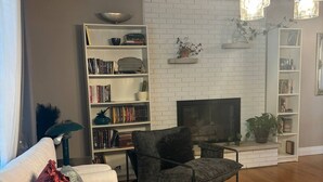 A modern living room with a white brick fireplace, a bookshelf, a sofa with decorative pillows, and a wooden coffee table. - Luxury Modern Stay - 2000 Sqft (Indianapolis)