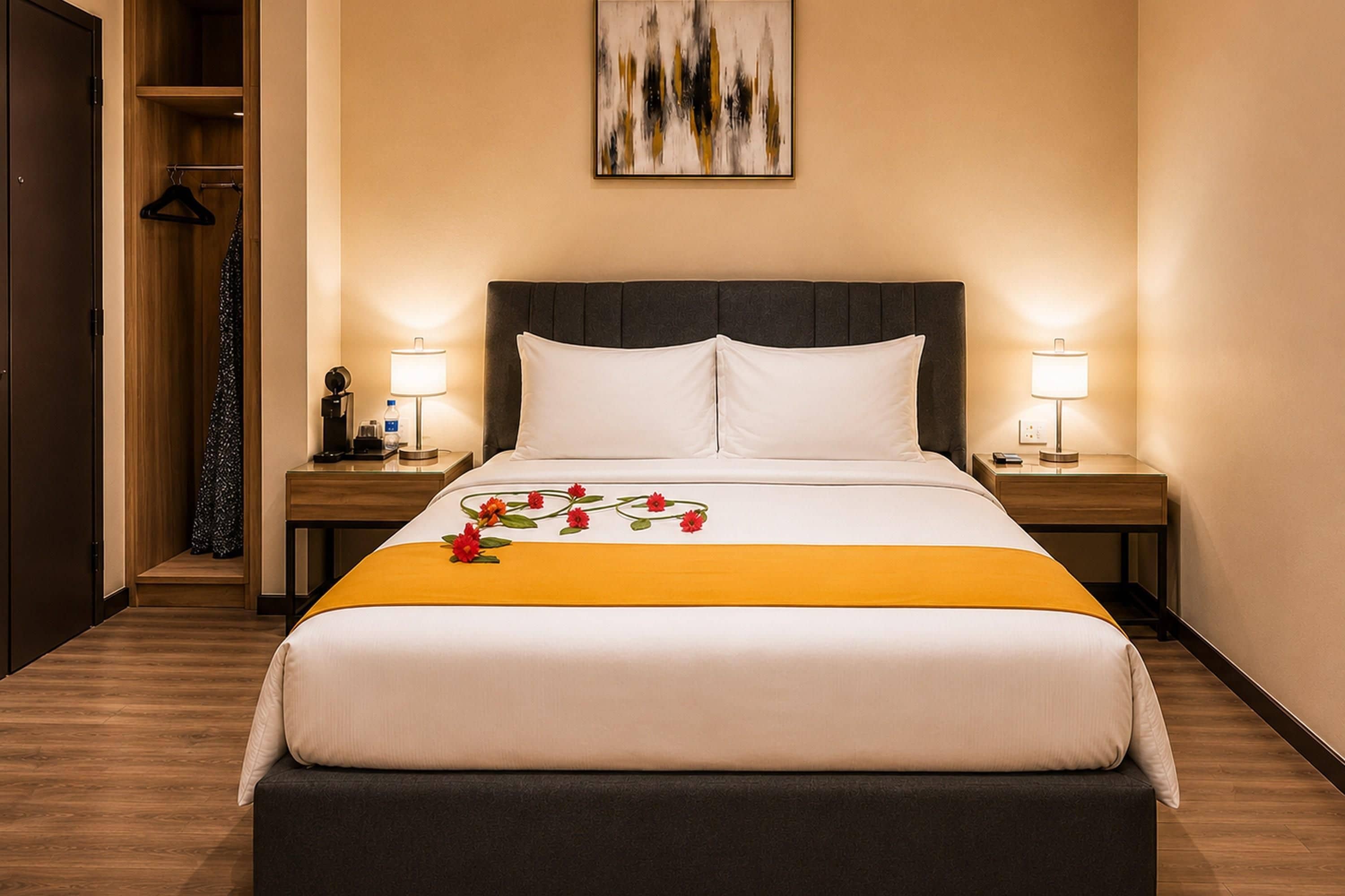 A hotel room with a bed, two bedside tables, a nightstand, a water dispenser, a lamp, and a painting on the wall.