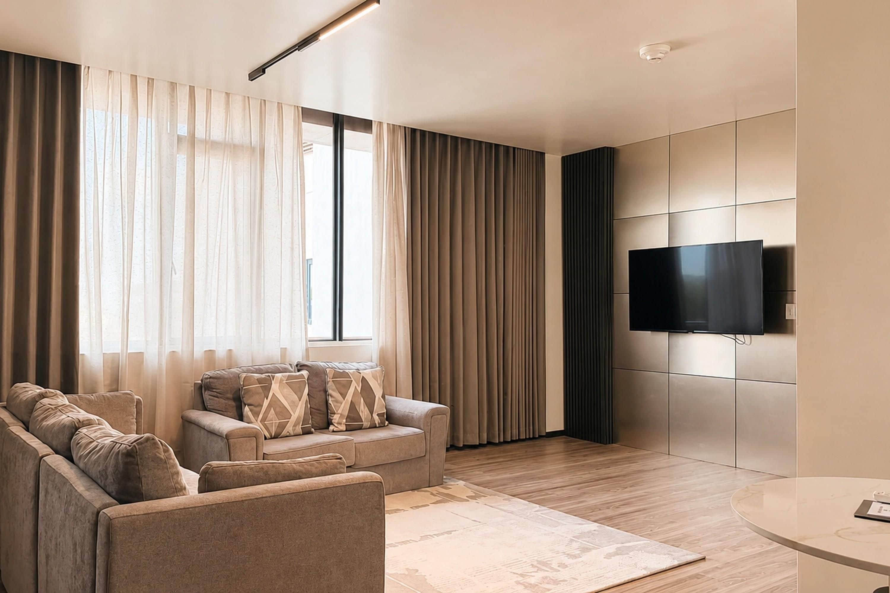 A modern living room with a sofa set, a flat-screen TV mounted on the wall, and a round coffee table.