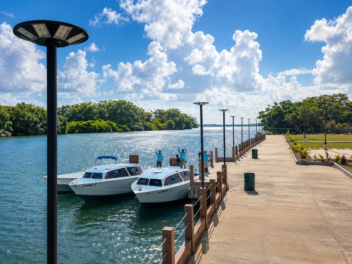 A waterfront dock with boats, a concrete walkway, and a row of street lamps.