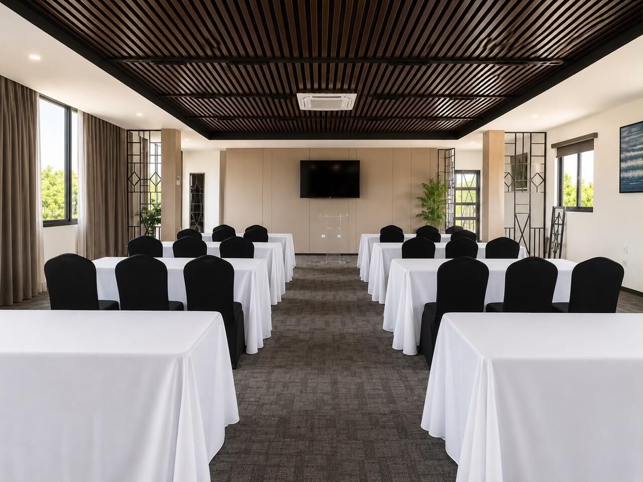 A conference room with rows of tables and chairs, a flat-screen TV, and a wooden ceiling.