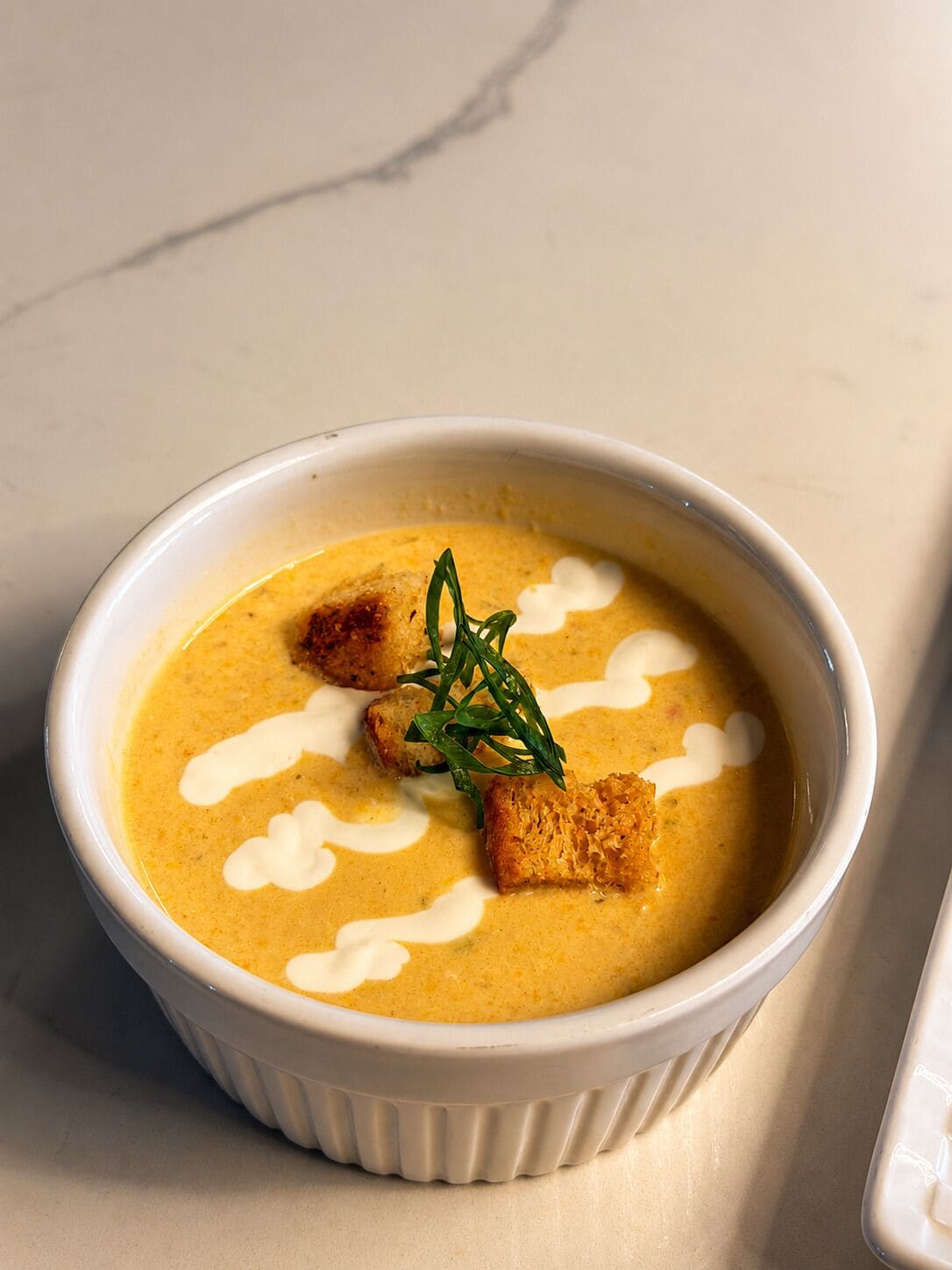 A bowl of soup with croutons and a garnish on a marble surface.