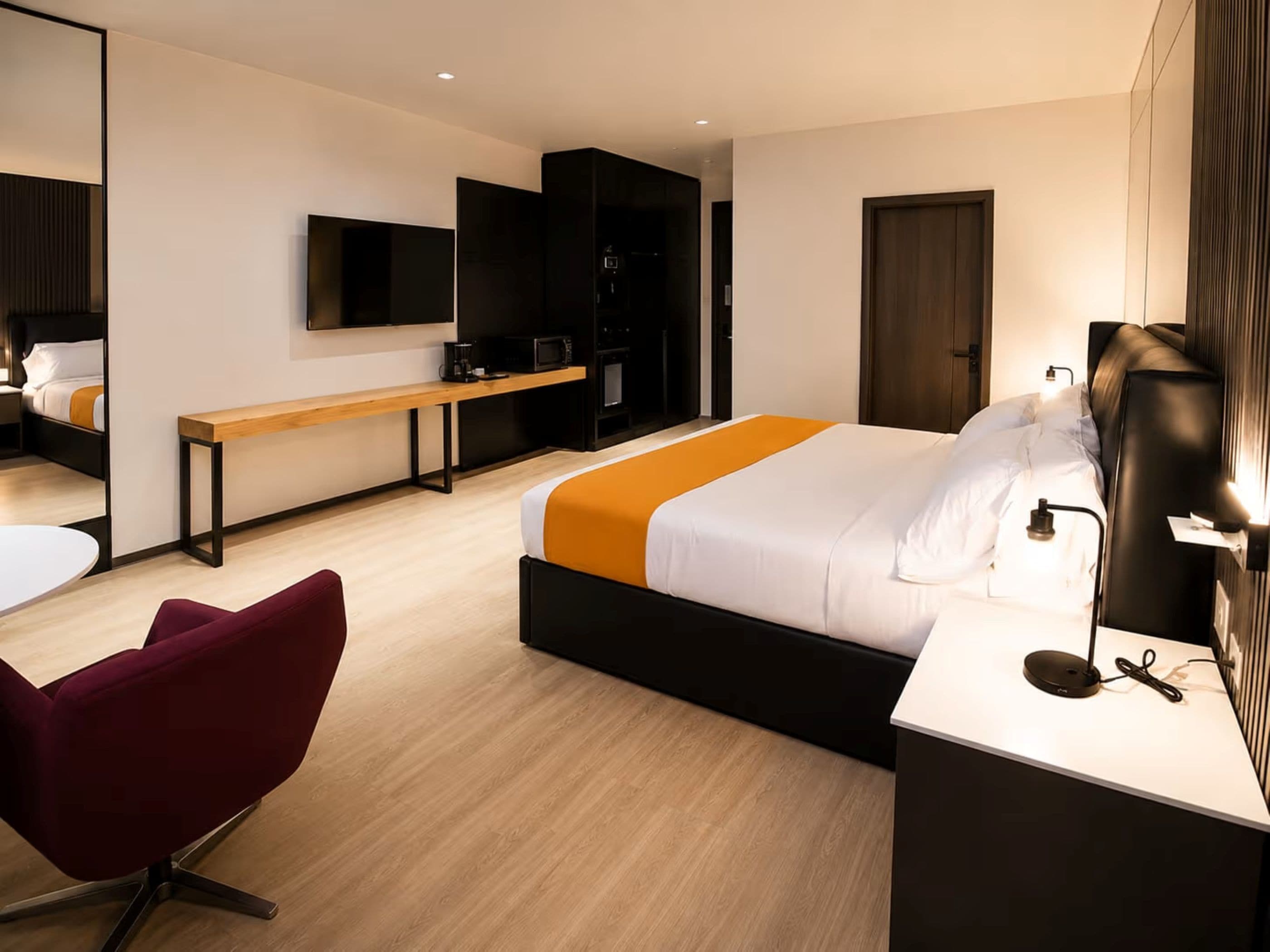 Ett modernt hotellrum med en säng, ett skrivbord, en stol, en bänk, en TV och en garderob.