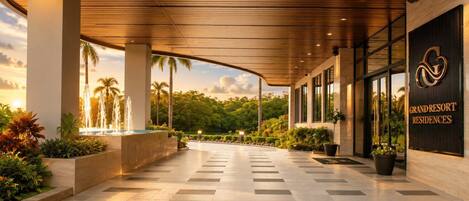 Imponente entrada de un resort con una fuente, palmeras y un letrero que dice 'GRAND RESORT RESIDENCES'.