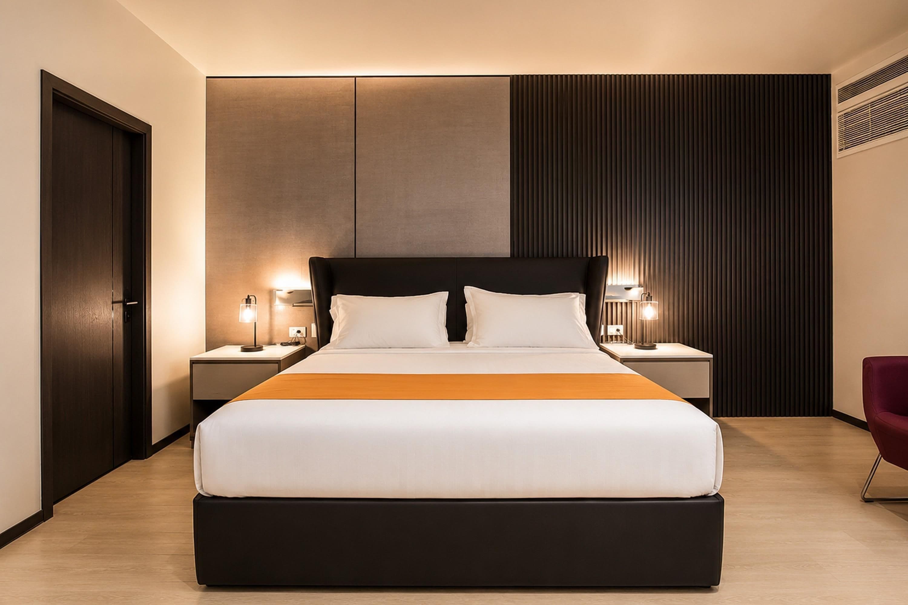Una habitación de hotel moderna con una cama grande, dos mesitas de noche con lámparas, un cabecero oscuro y suelo de madera.
