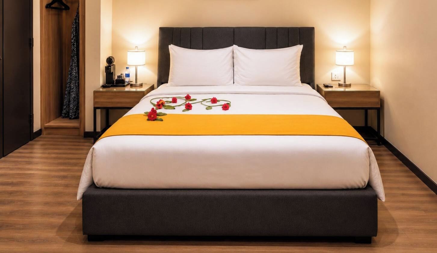 Een hotelkamer met een groot bed, twee nachtkastjes met lampen, een houten vloer en een donker hoofdeinde.