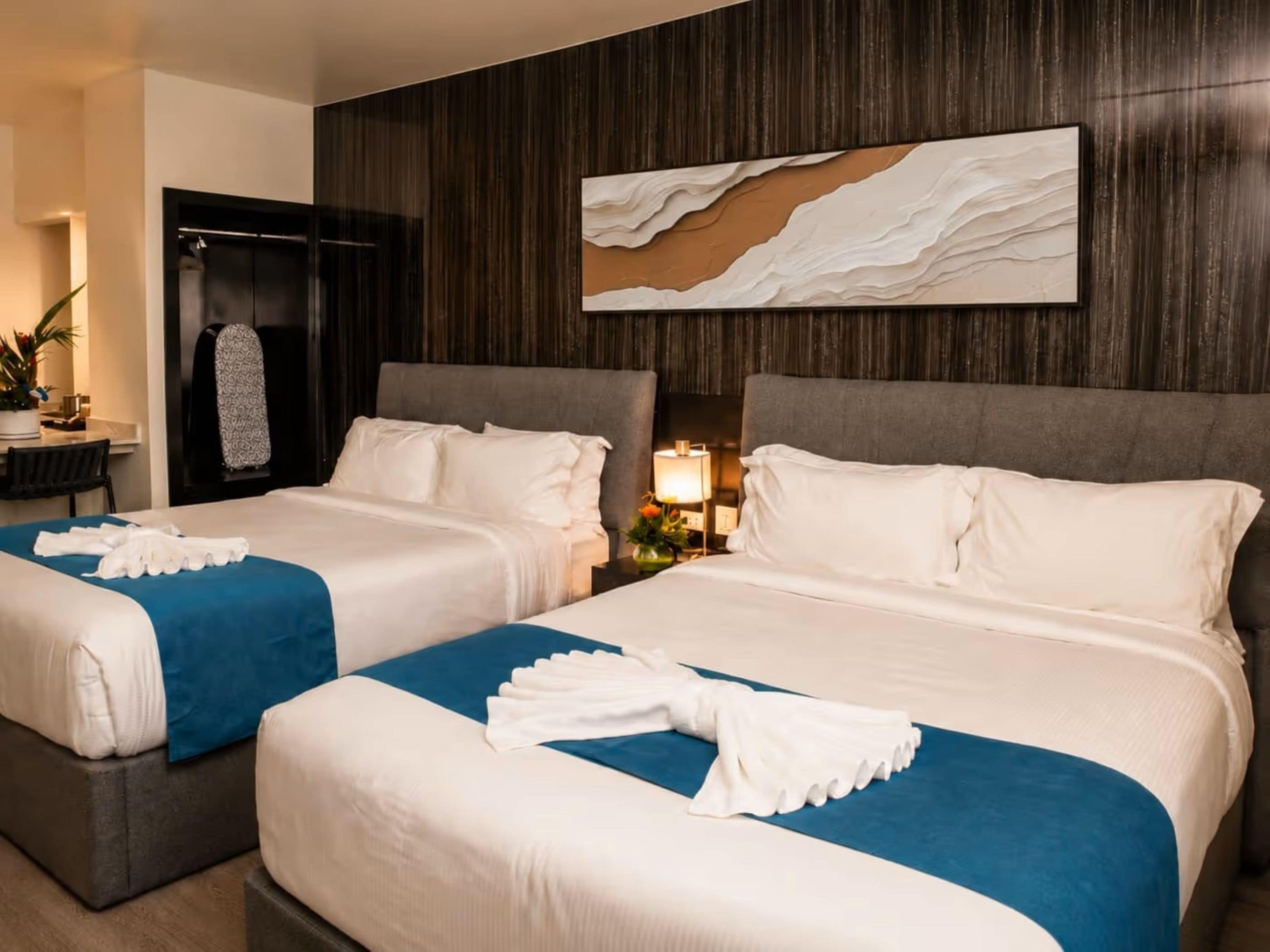 Habitación de hotel con dos camas, un cuadro abstracto grande en la pared y un escritorio con lámpara.