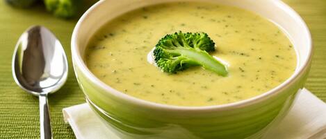 Un tazón de sopa verde con una guarnición de brócoli sobre un mantel verde.