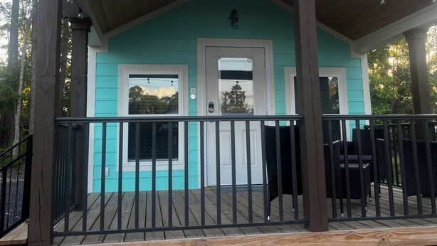 A covered outdoor area with a wooden deck, a railing, and a door with windows. - Cozy pet friendly 2-bedroom cabin in tranquil Steinhatchee (Steinhatchee)
