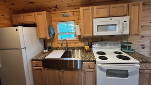 A kitchen with wooden cabinets, a stainless steel sink, a white refrigerator, a white stove, and a microwave. - Cozy pet friendly 2-bedroom cabin in tranquil Steinhatchee (Steinhatchee)