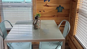 A dining area with a wooden wall, a glass table, and two light blue chairs. - Cozy pet friendly 2-bedroom cabin in tranquil Steinhatchee (Steinhatchee)
