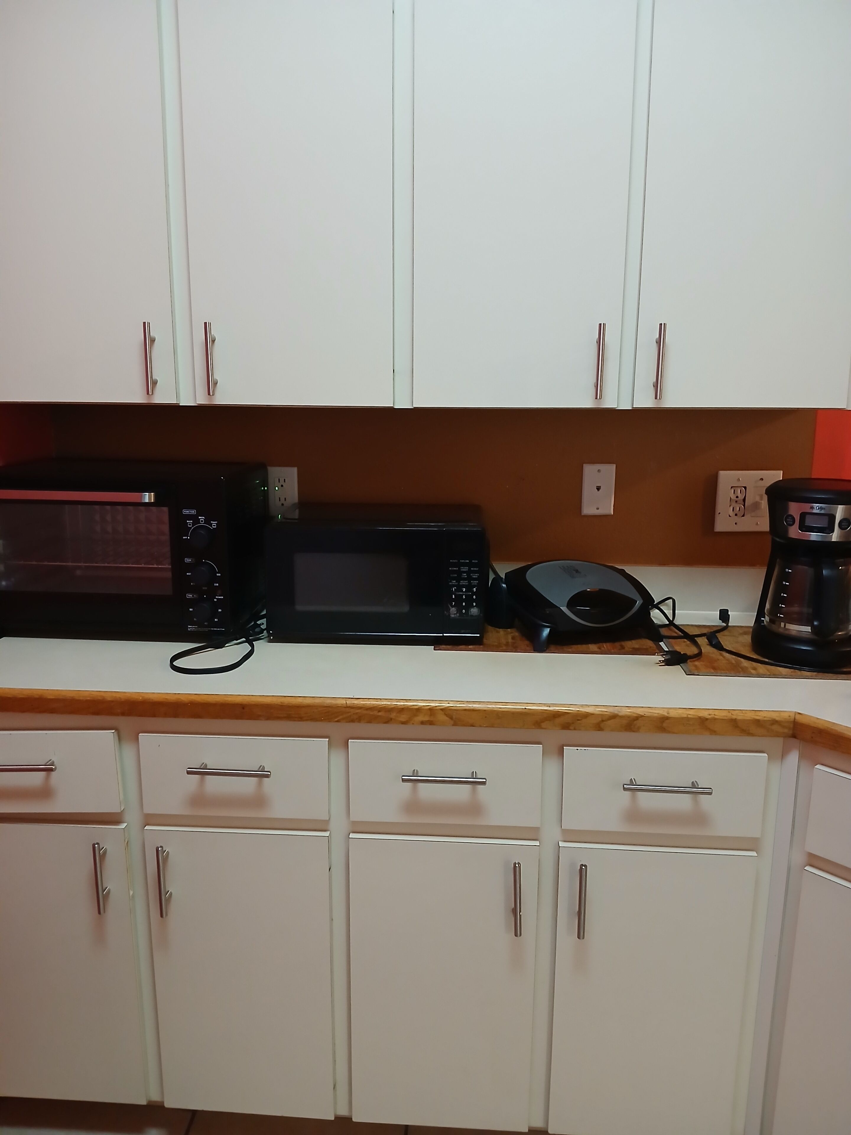 A kitchen with white cabinets, a microwave, a coffee maker, and a toaster.