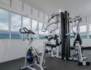 Academia com máquinas de cardio, equipamentos de musculação, janelas amplas e vista para o horizonte urbano.