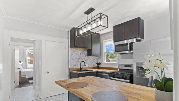 Une cuisine moderne avec des meubles de couleur sombre, un îlot central en bois, des appareils électroménagers en acier inoxydable et une vue sur l’extérieur.