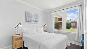 Une chambre à coucher avec un grand lit, deux tables de chevet avec des lampes, un tableau au mur et une fenêtre avec des rideaux.