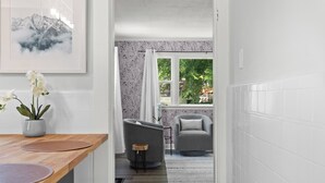 Un intérieur moderne avec une table à manger en bois, un fauteuil gris et une vue sur un jardin par la fenêtre.
