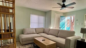 A living room with a sectional sofa, a coffee table, a bookshelf, and a ceiling fan.