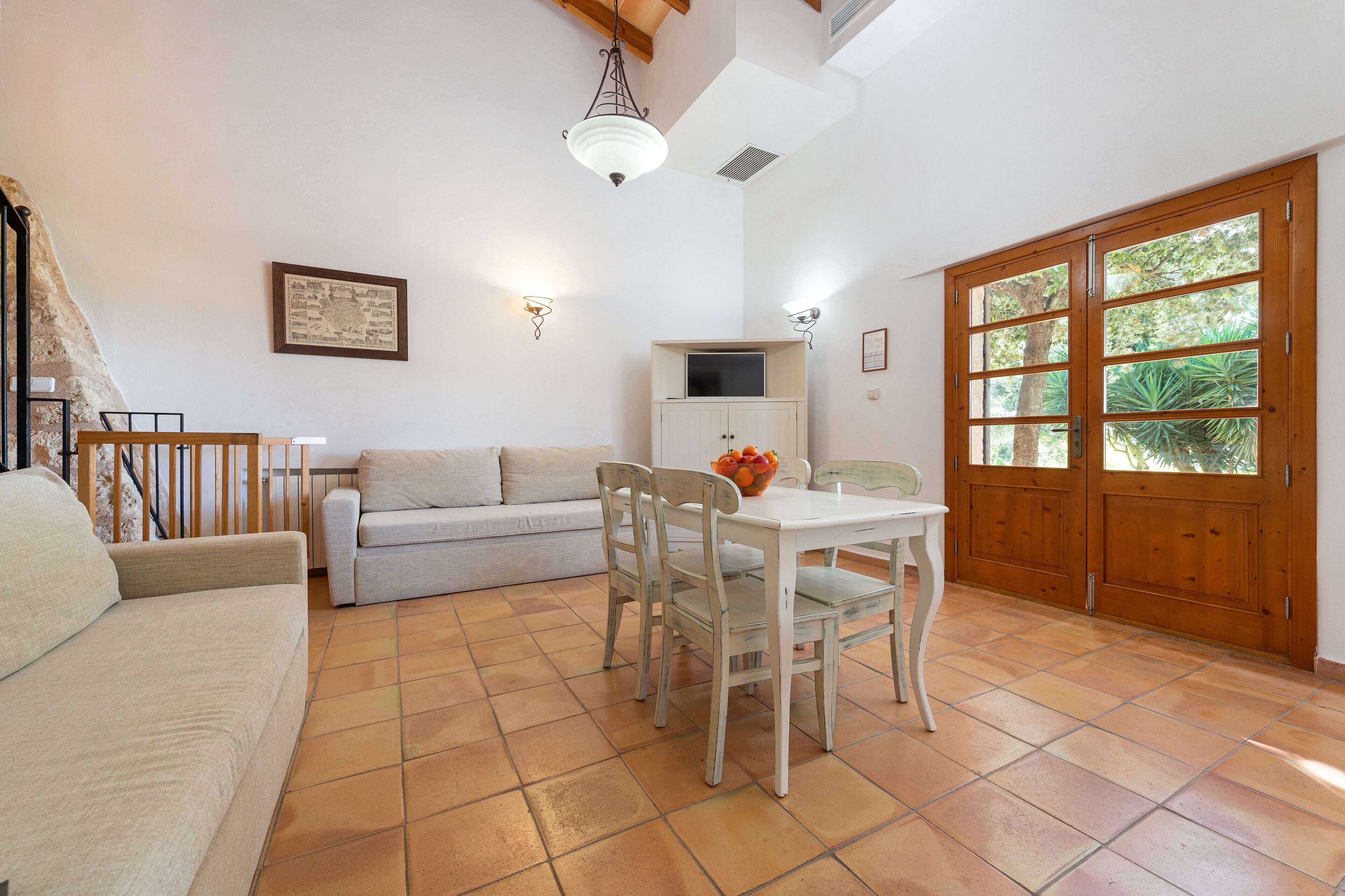 A living room with a sofa, a dining table with chairs, a TV on a cabinet, and a wooden door with glass panels.