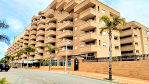 A multi-story apartment building with balconies, a commercial building entrance, and palm trees. - ACV - Costa Azahar I-2nd line 3rd floor 3 north 2 (OROPESA)