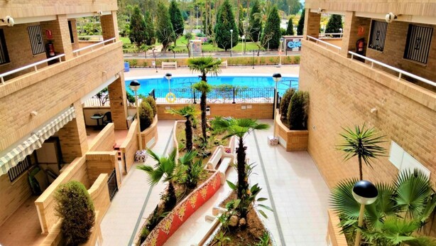 A courtyard with a swimming pool, surrounded by brick buildings, featuring outdoor seating and potted plants. - ACV - Costa Azahar I-2nd line 3rd floor 3 north 2 (OROPESA)