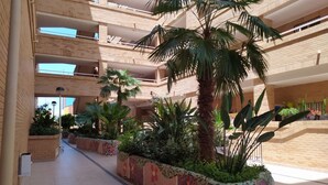 A multi-level atrium with a central walkway, surrounded by planters with various plants and flowers. - ACV - Costa Azahar I-2nd line 3rd floor 3 north 2 (OROPESA)