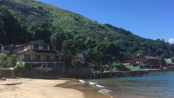 Uma praia com areal, um barco pequeno e casas com uma colina ao fundo.