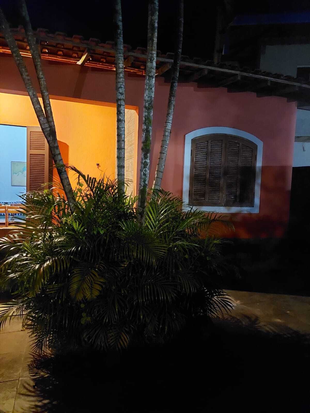 A building with a red facade, a window with shutters, and a potted plant with broad leaves.