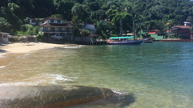 A beach with clear water, a rocky foreground, and houses in the background. - Angra dos Reis - Beachfront House - Praia de Fora - East End (Unknown)