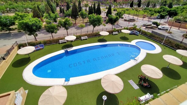 Une piscine appelée « COSTA AZAHAR I », entourée d’une pelouse verdoyante et de parasols blancs.