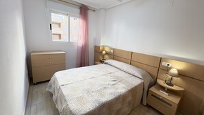 Une chambre à coucher comprenant un lit, des tables de chevet, une commode, un ventilateur de plafond et une fenêtre avec un rideau.