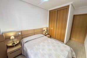 Un dormitorio con una cama, dos mesitas de noche con lámparas, un armario de madera y una puerta de madera.