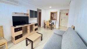 Un salon moderne doté d’un téléviseur à écran plat, de meubles en bois, d’un canapé gris et d’un coin repas avec des chaises et une table.