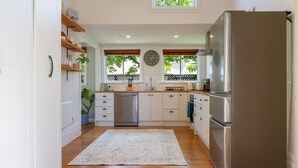 A modern kitchen with white cabinets, a stainless steel refrigerator, and a clock on the wall. - Exclusive 2 Bed Standalone Villa in St Albans (Christchurch)