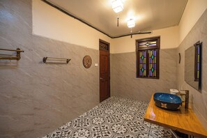 A bathroom with a wooden vanity, a blue basin, patterned floor tiles, a door, and a stained glass window. - Penang Story Linn House (George Town)