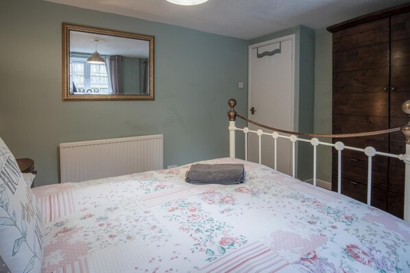 A bedroom with a bed, a wooden wardrobe, a white radiator, and a mirror on the wall.