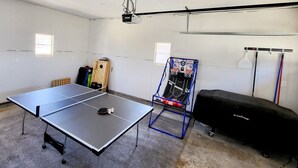 Une table de ping-pong dans une pièce équipée d’un projecteur, d’un panier de basket et d’un système audio.