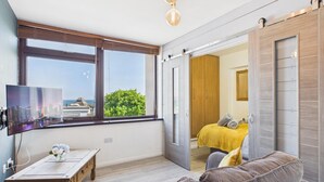 A bedroom with a bed, a TV, a window with a cityscape view, and a door leading to another room.
