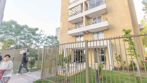 Un edificio de varios pisos con balcones, una entrada protegida por una reja y un pequeño jardín.