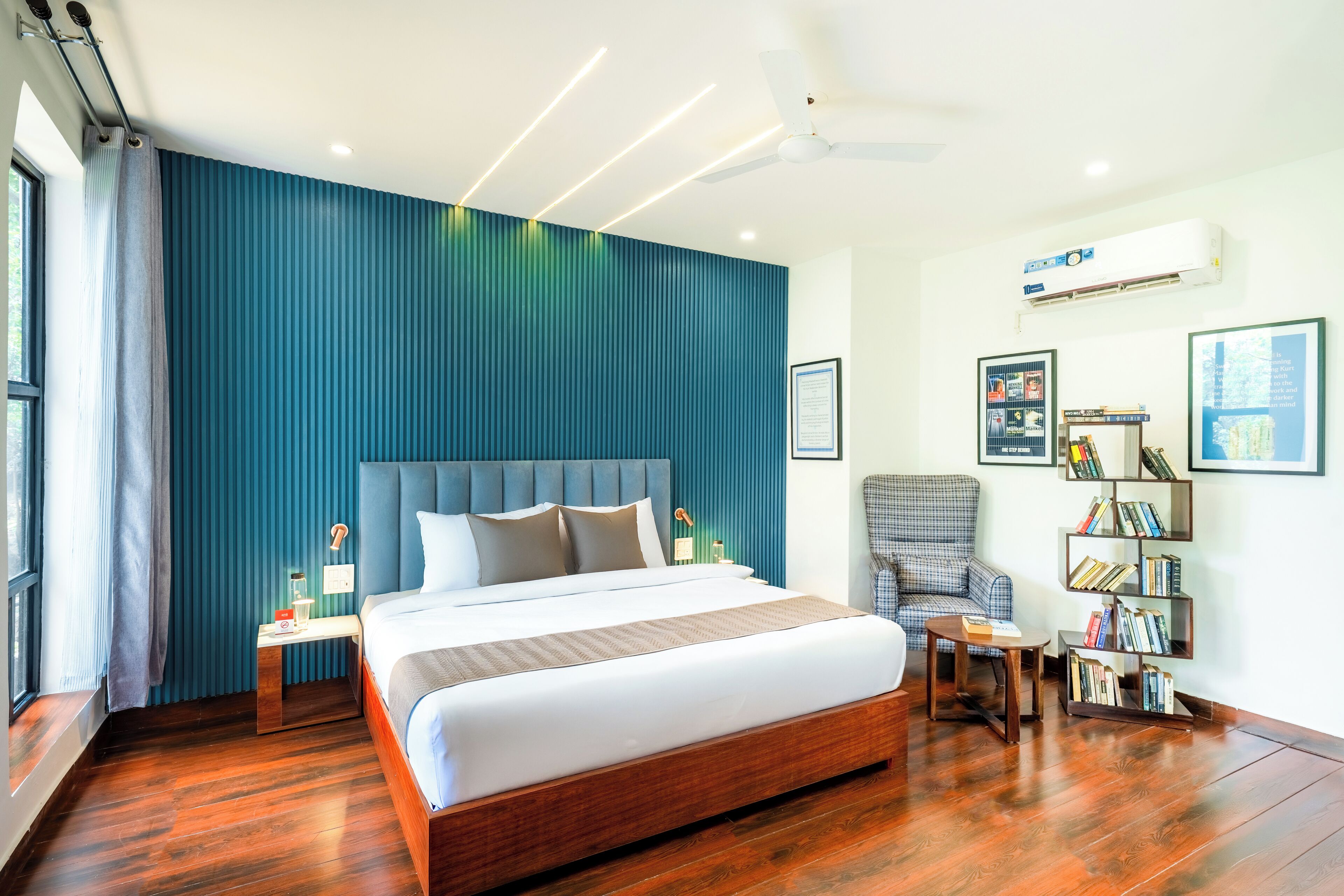 Una habitación de hotel moderna con una cama grande, un área de descanso con una silla, una mesita y una estantería.
