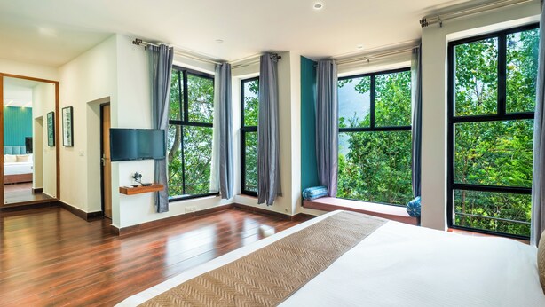 A modern hotel room with large windows, a bed, a TV, and a view of the outdoors. - amã Stays & Trails Writer's Hill Nahan, Sirmaur Himachal (Nahan)