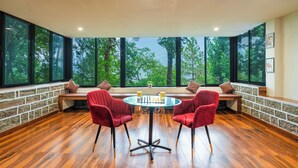 A room with a large window, a round table, and two red chairs. - amã Stays & Trails Writer's Hill Nahan, Sirmaur Himachal (Nahan)