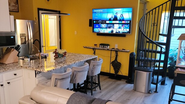 A modern kitchen with a built-in refrigerator, a dining area with a marble countertop, and a TV mounted on the wall displaying a streaming service interface. - Houston Sweet spot Town house in shadows of downtown skyscrapers' w/rooftop view (Houston)