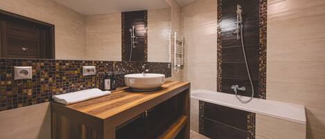 A modern bathroom with a wooden vanity, a white sink, a large mirror, a bathtub, and a shower.