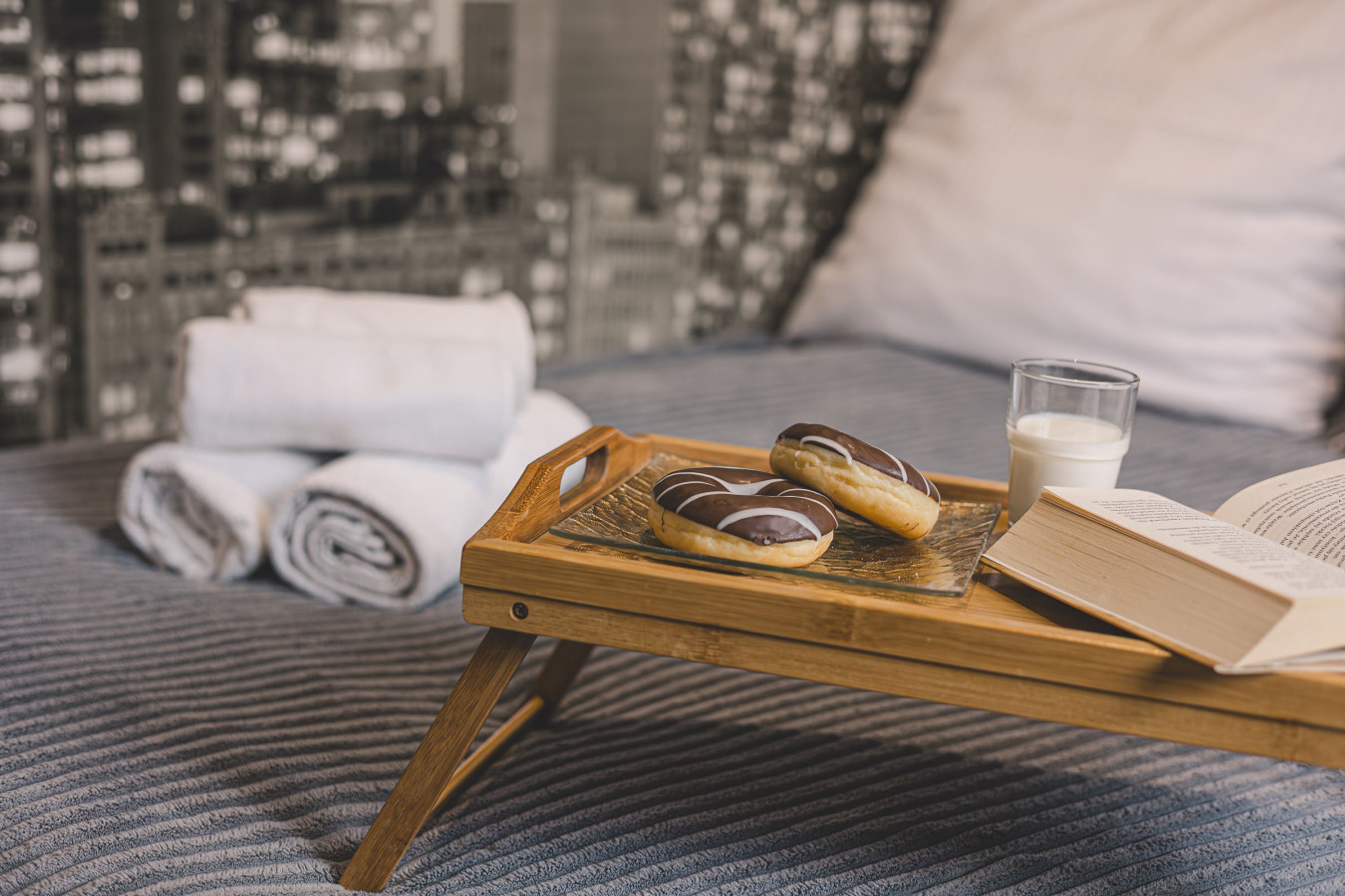 Ein Bett mit Blick auf die Stadt, ein Tablett mit Gebäck und ein Glas Milch sowie ein Buch auf einem kleinen Holztisch.