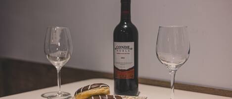 Two wine glasses, a bottle of Conde Noble wine, and two chocolate-covered donuts on a table.