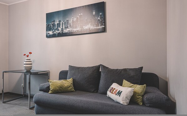 A modern living room with a grey sofa, a small side table, and a cityscape painting on the wall. - Dream 23B Apartment Nowoczesne Studio w Centrum (Bydgoszcz)